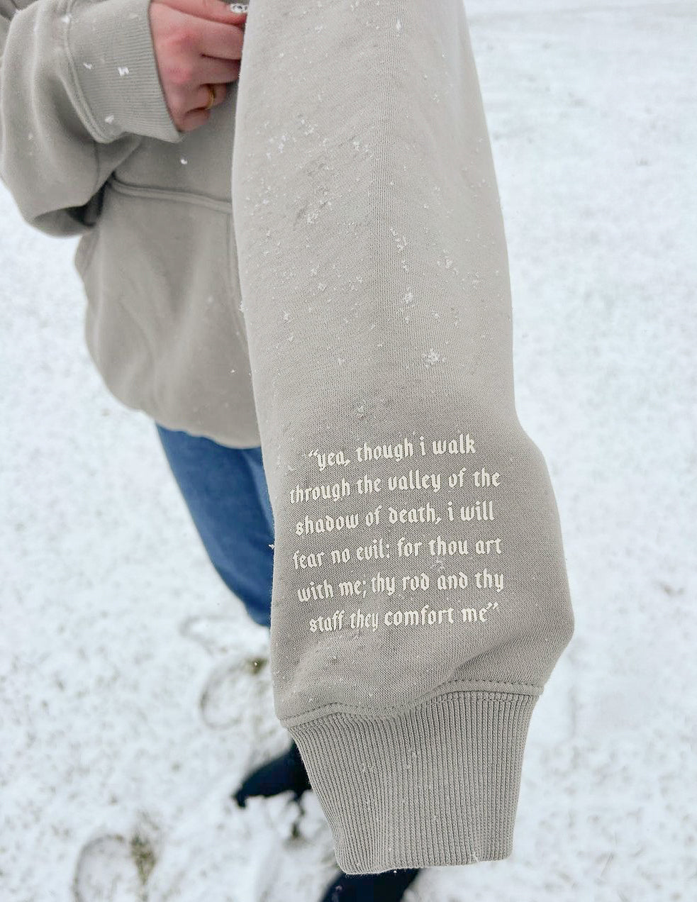 Grey hoodie sleeve with quote print and ribbed cuff; hoodie hem visible.