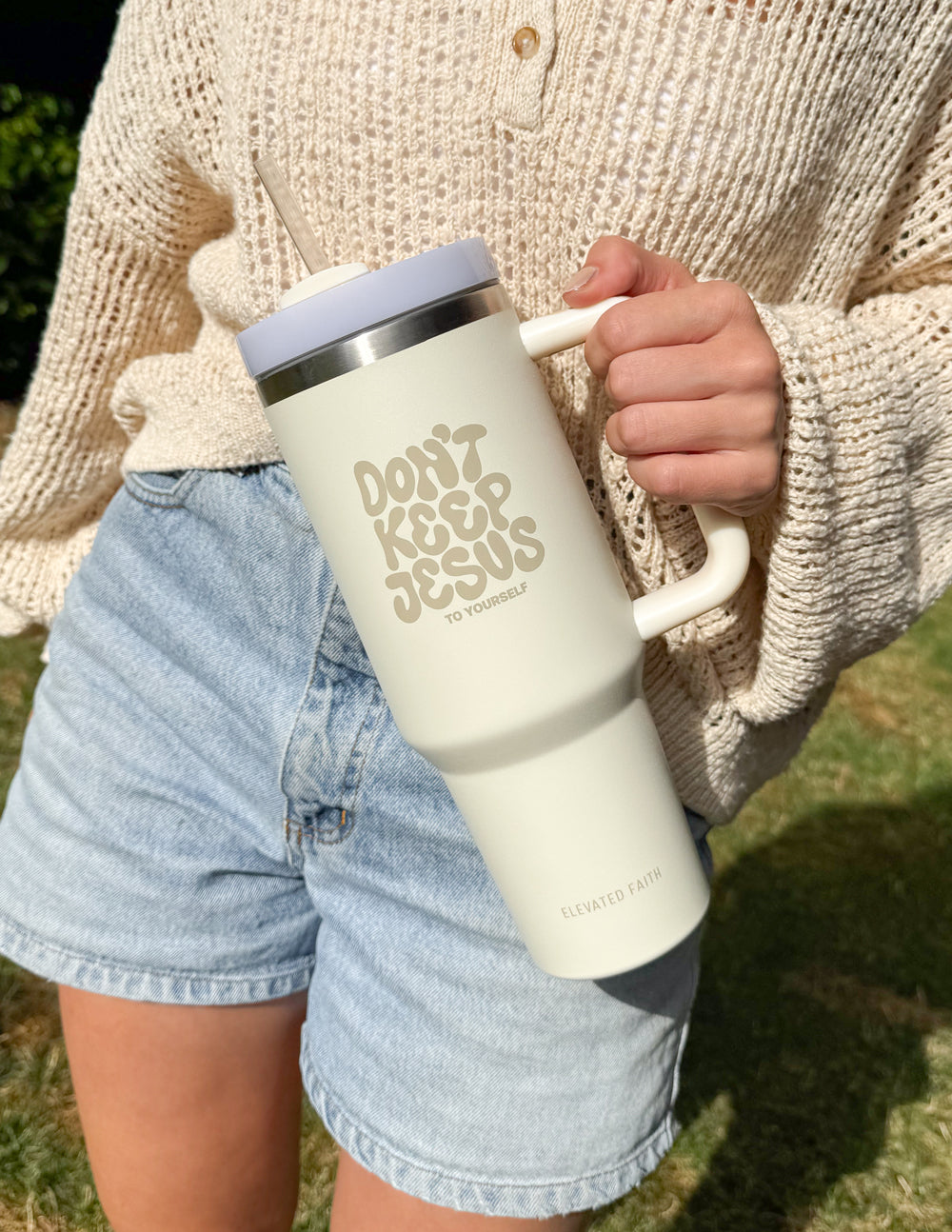 Cream travel tumbler with silver lid, straw, and side handle held in hand