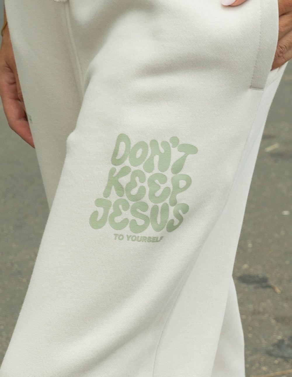 Cream unisex sweatpants with large green “Don’t Keep Jesus” logo print