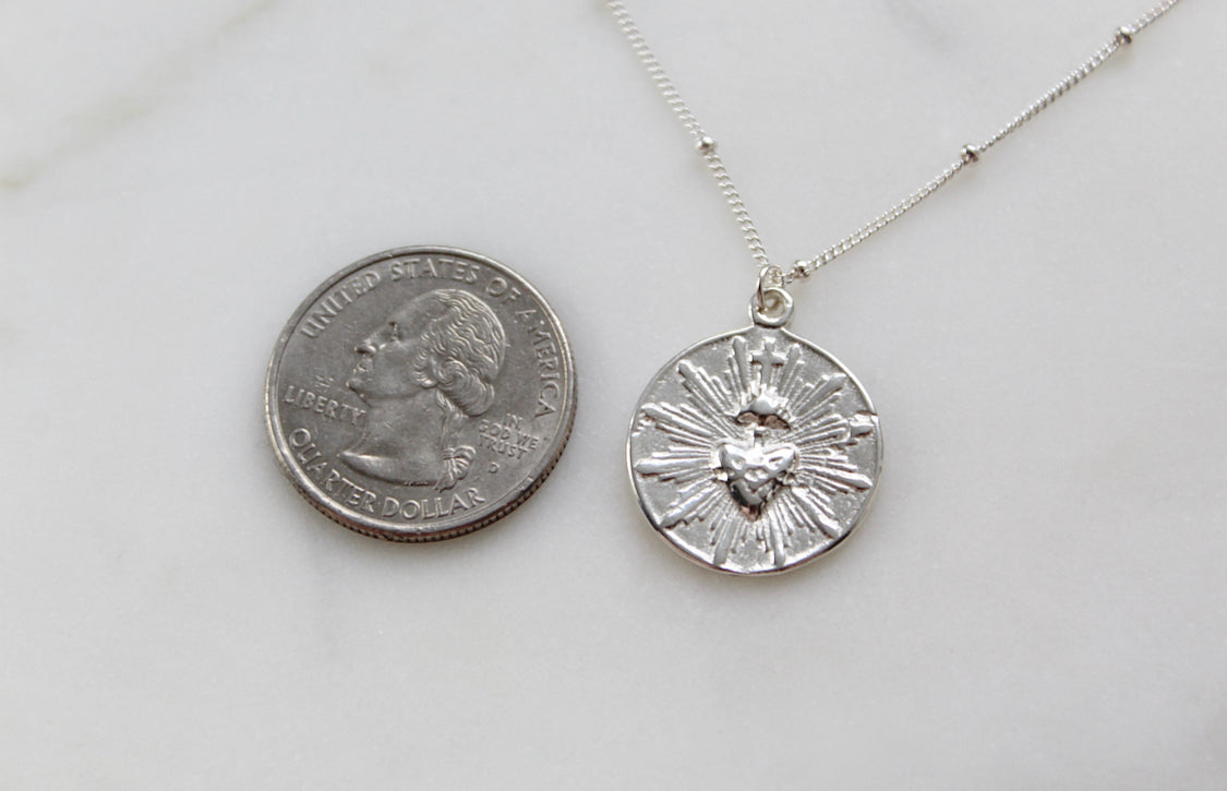 Silver sacred heart coin pendant on fine chain, beside a coin for size.