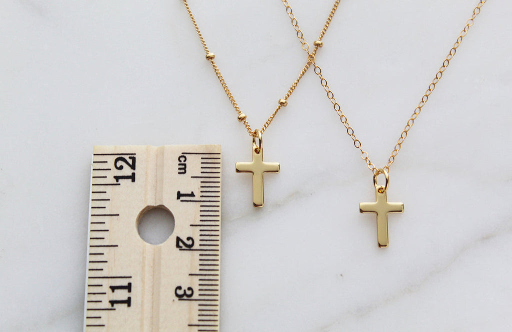 Gold cross pendant necklaces next to measuring tape, small cross charms on chains