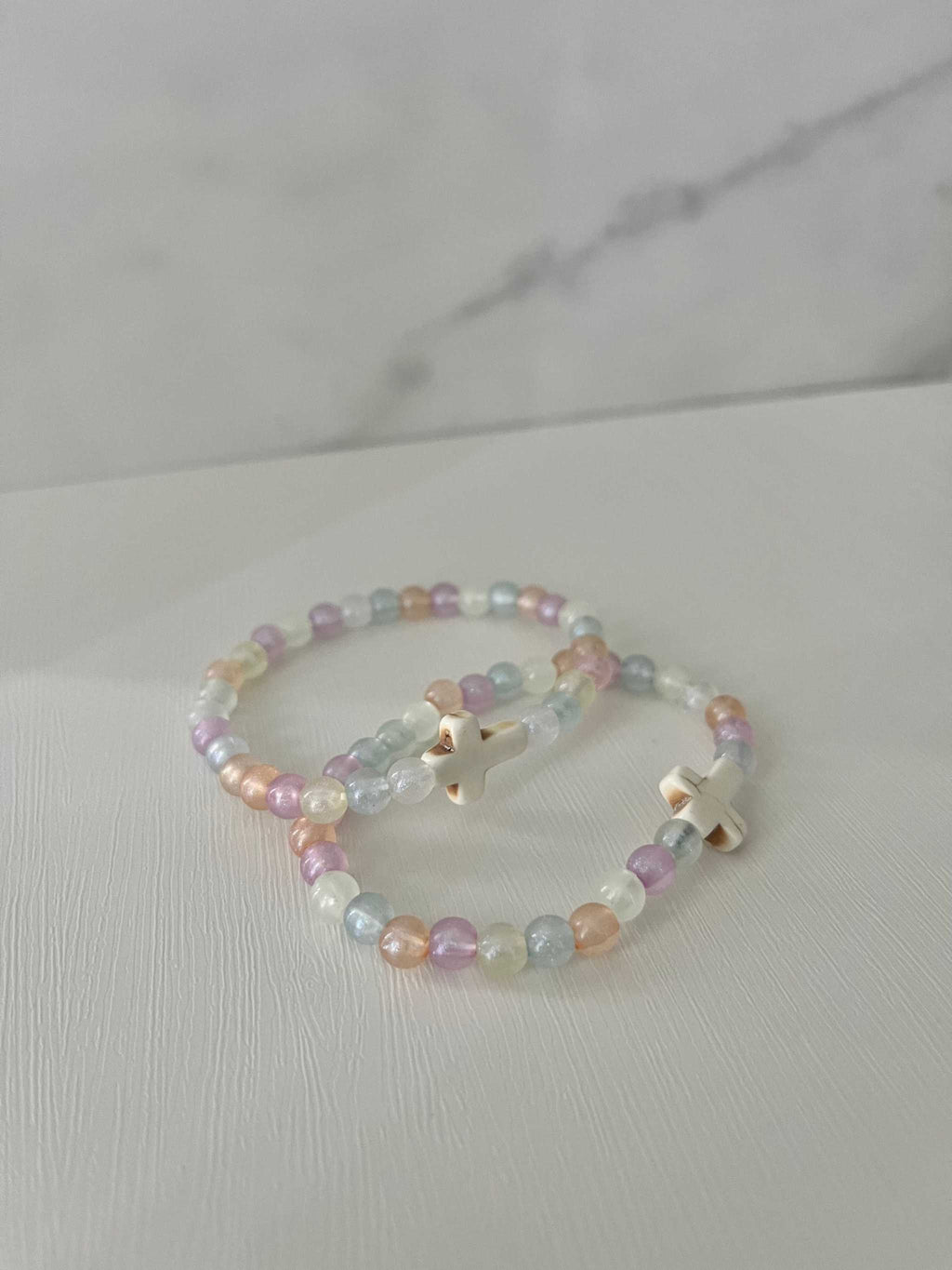 Two overlapping pastel bead bracelets with white cross charms and small beads.