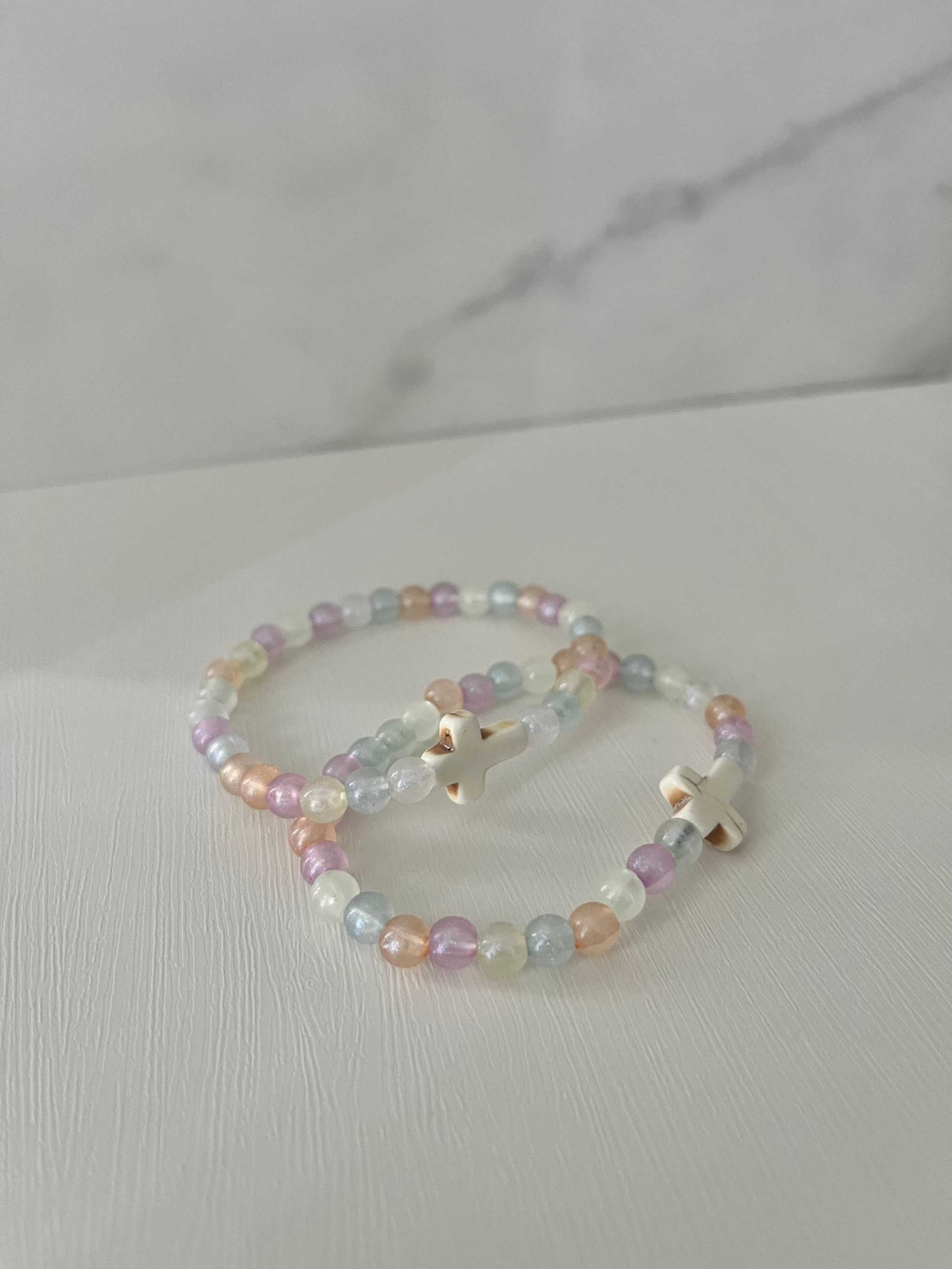 Two overlapping pastel bead bracelets with white cross charms and small beads.
