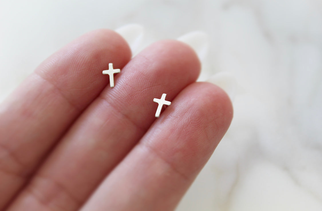 Sterling silver cross stud earrings on open palm, two cross charms visible.