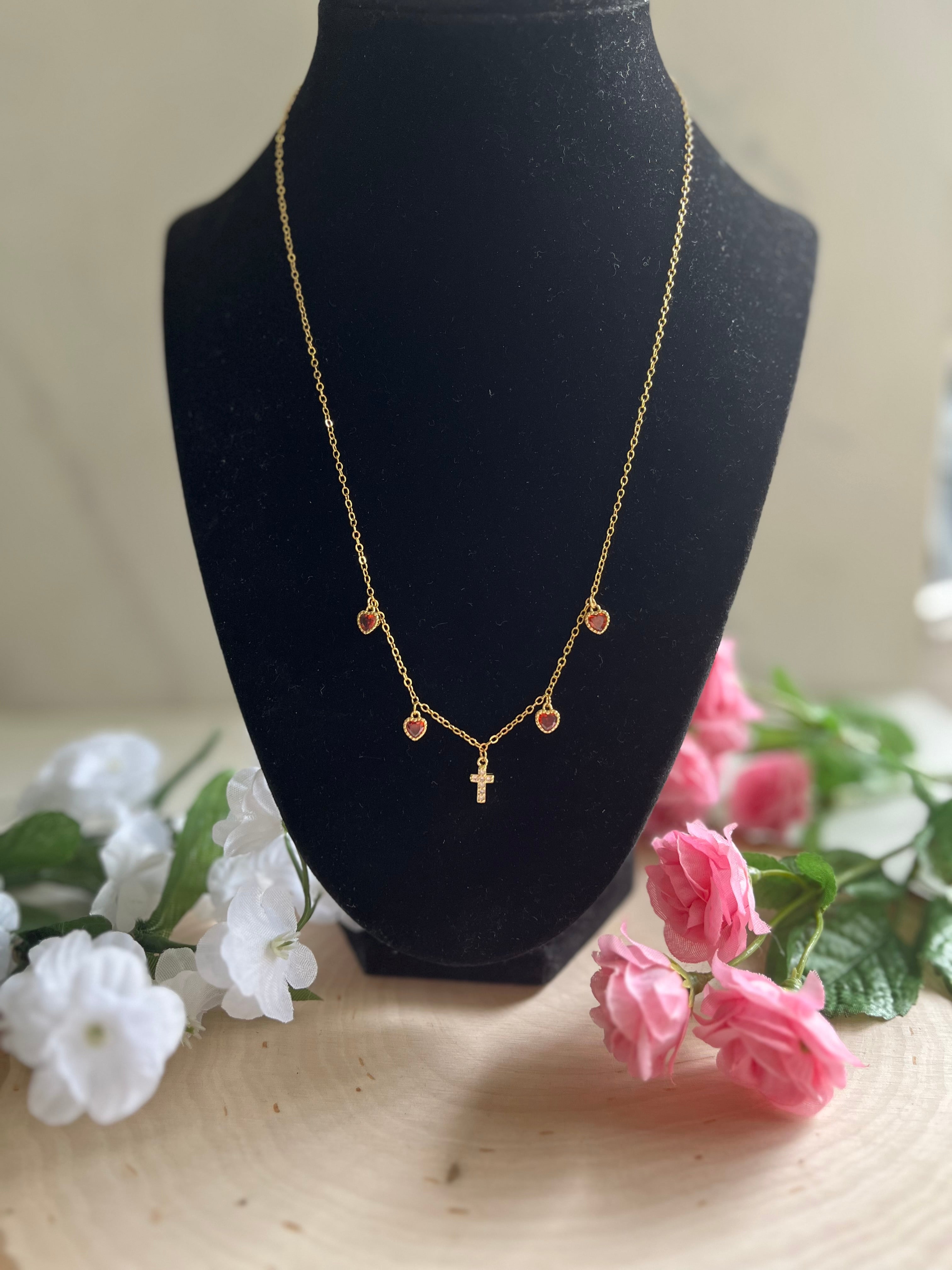 Gold charm necklace with red heart charms and gold cross pendant, front view
