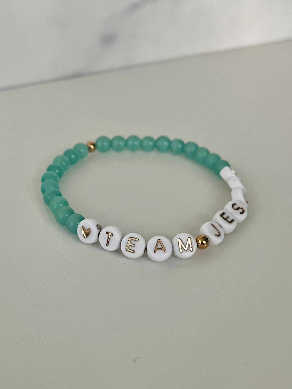 Teal iridescent beaded bracelet with white letter charms spelling TEAM