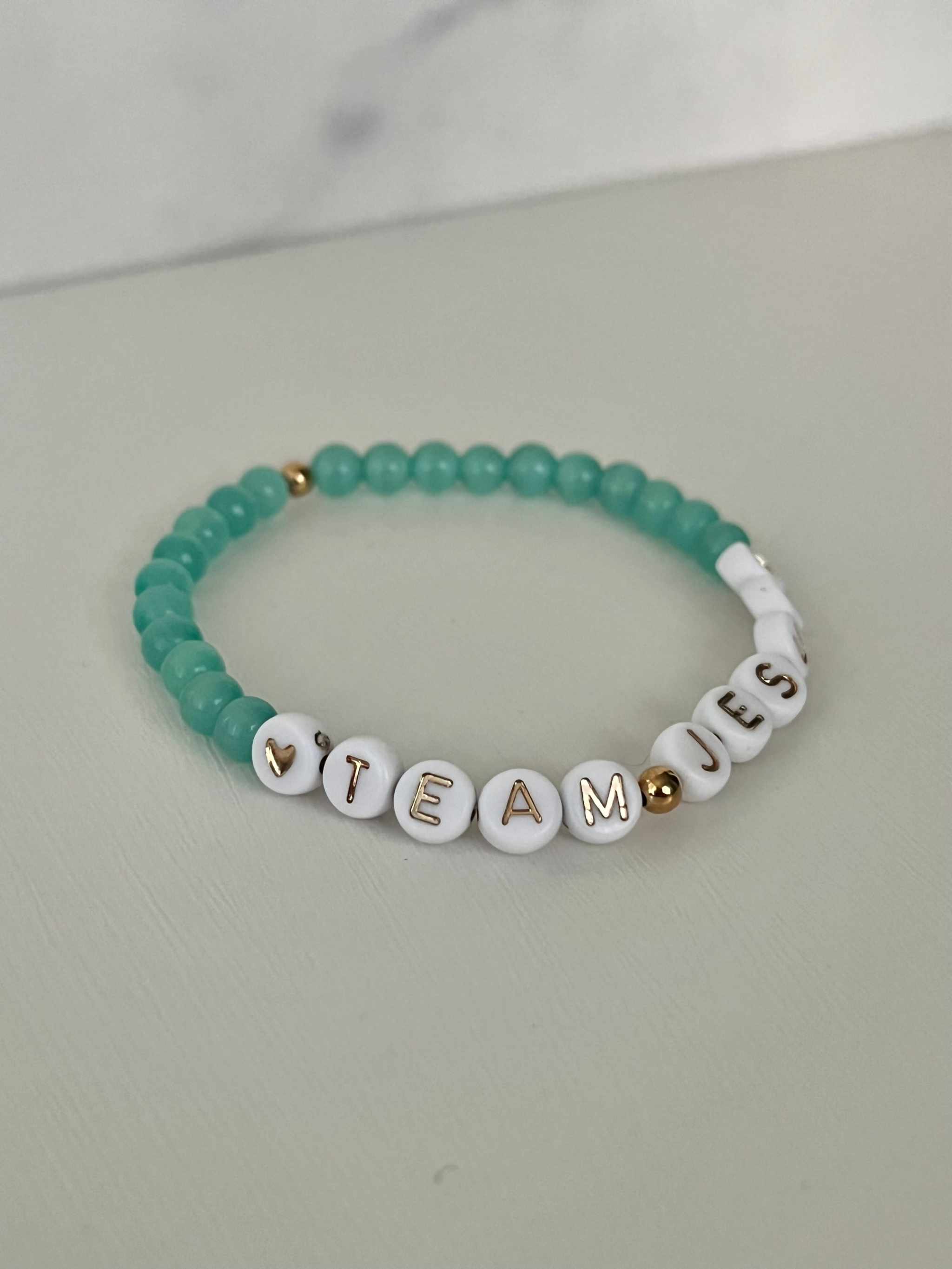 Teal iridescent beaded bracelet with white letter charms spelling TEAM