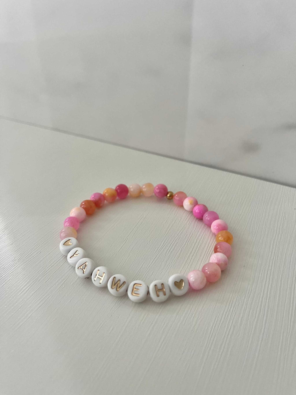 Pink beaded stretch bracelet with white letter charms spelling YAHWEH and heart accents.