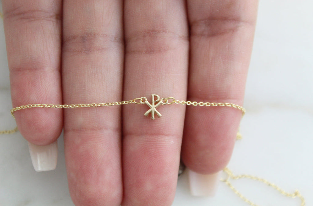 14K gold Chi Rho pendant on a fine chain, shown across the palm