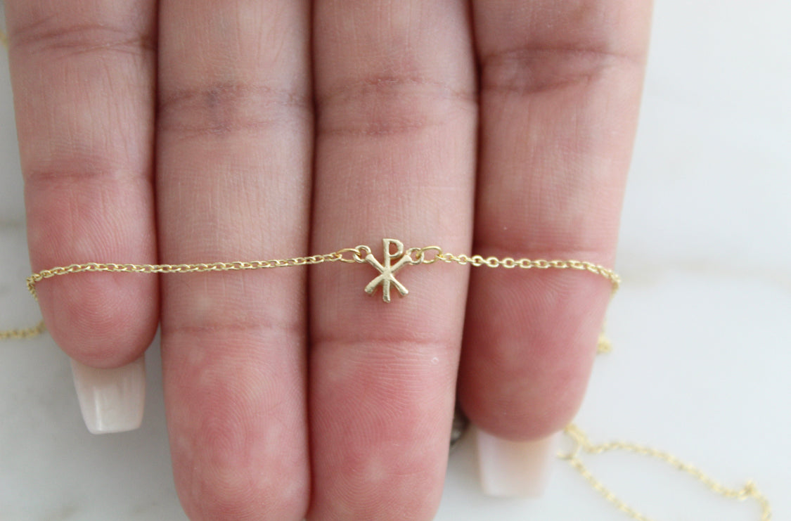 14K gold Chi Rho pendant on a fine chain, shown across the palm