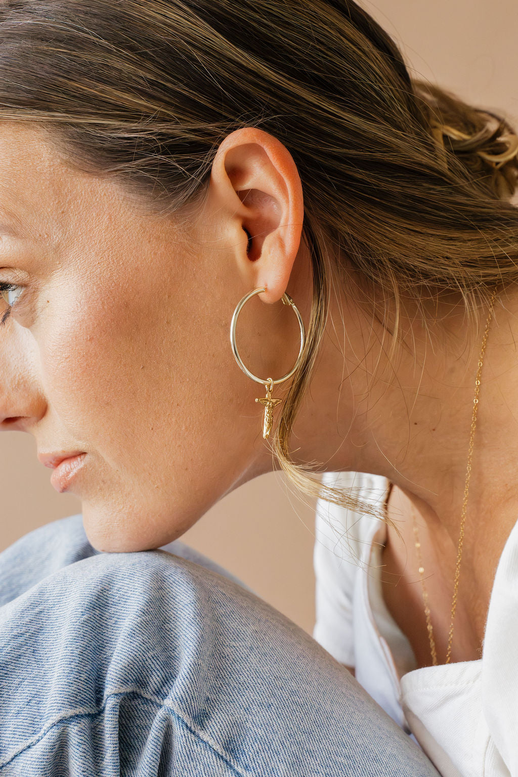 Gold-tone hoop earring with crucifix cross charm on ear