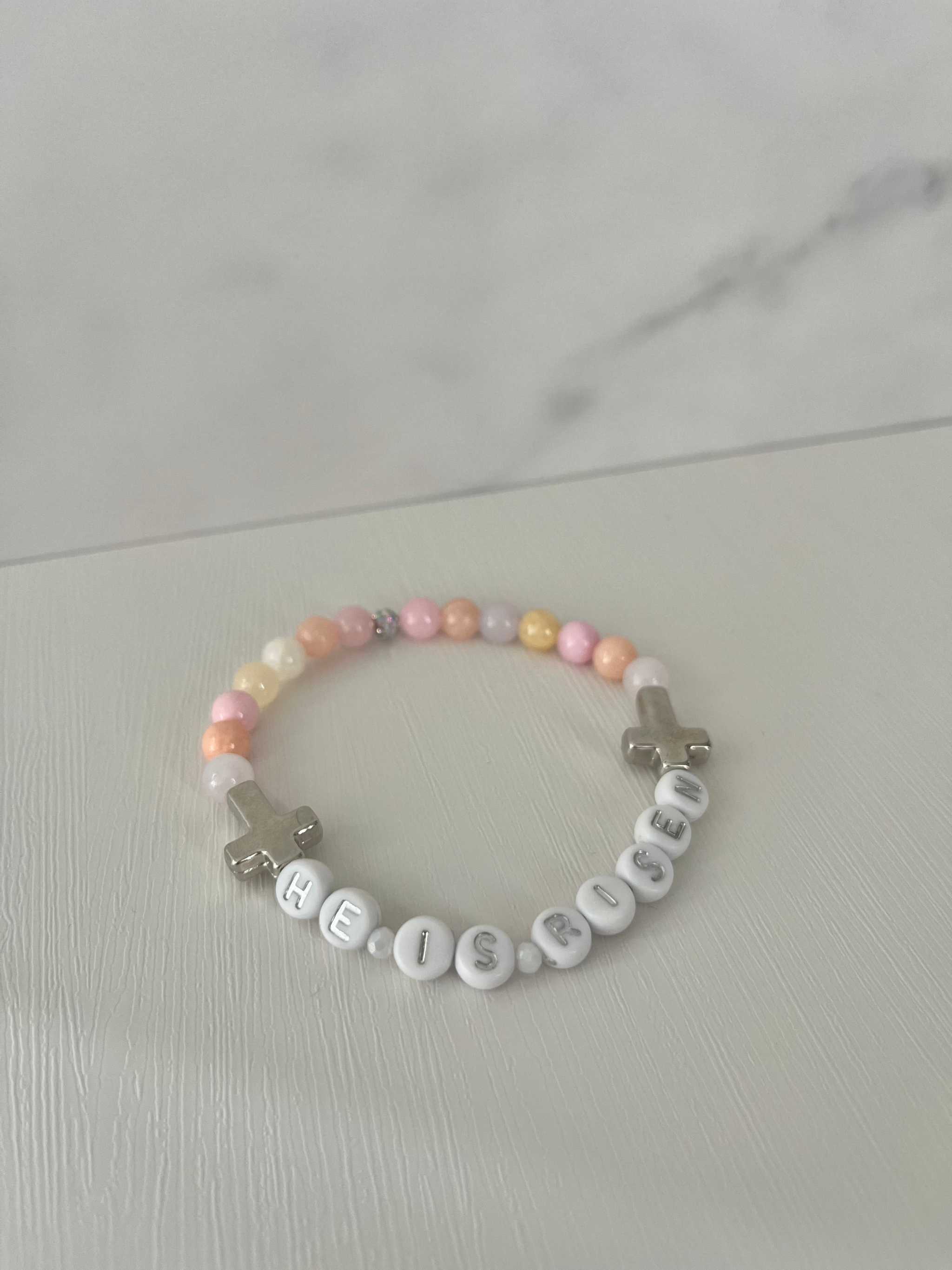 Pastel pink and white bead bracelet with 'HE IS RISEN' letter beads and silver cross charm