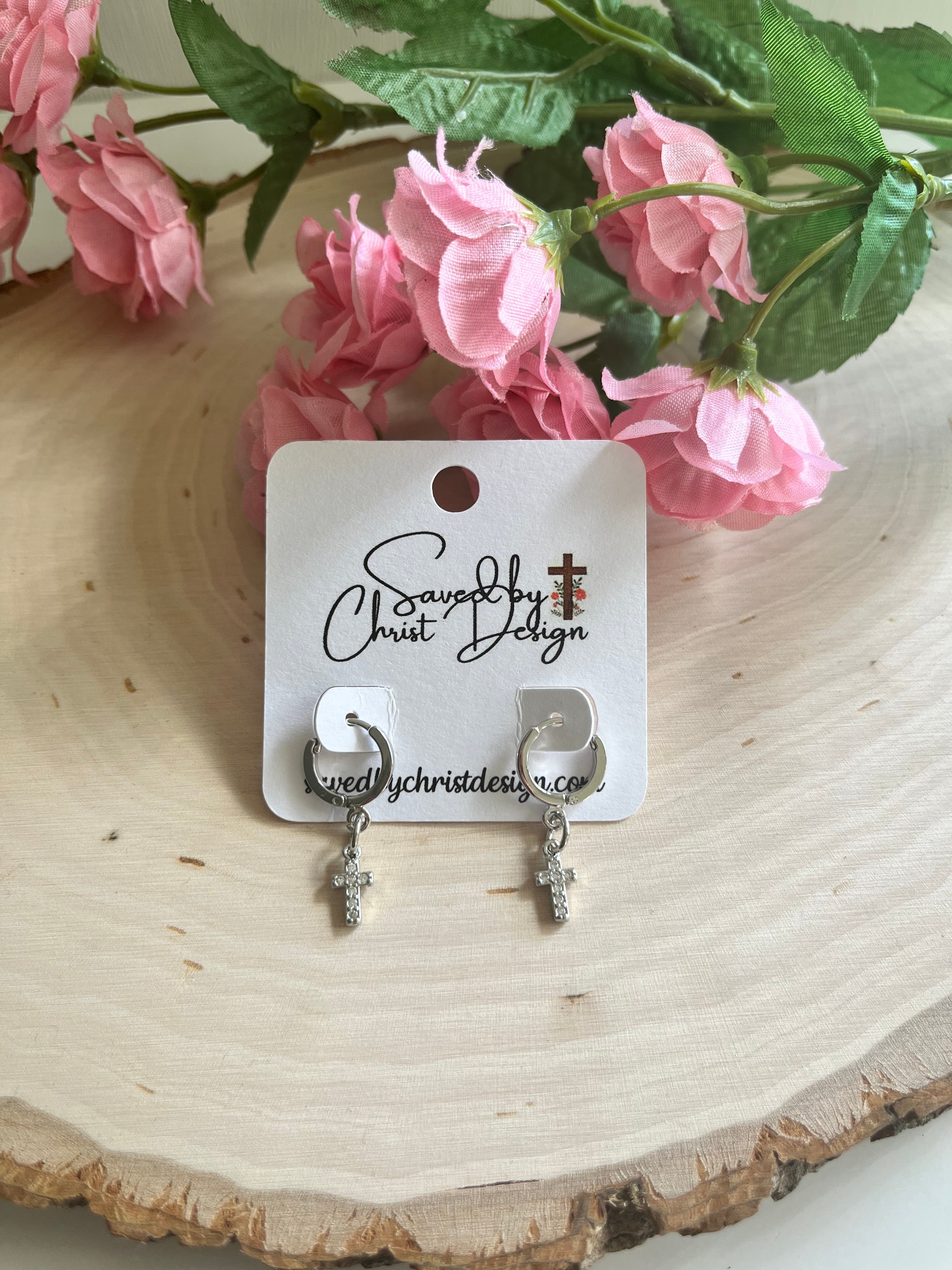Silver huggie hoop earrings with cross charms, dangling from small hoops