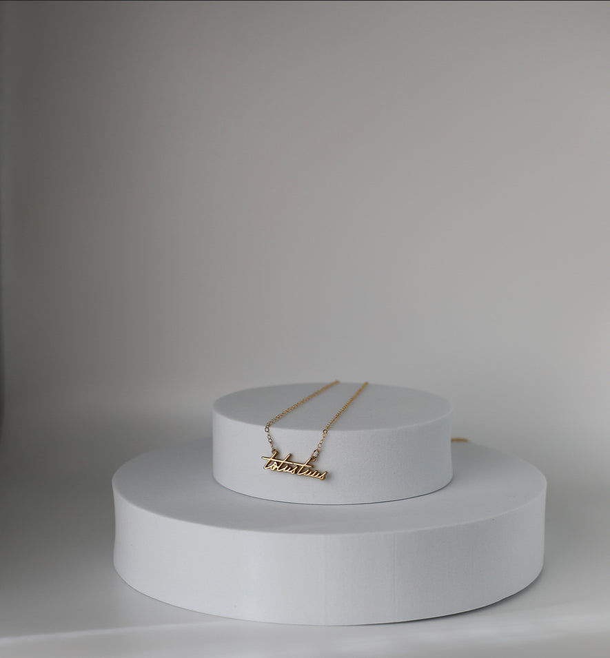 Gold-tone necklace with Totus Tuus script pendant on a display stand