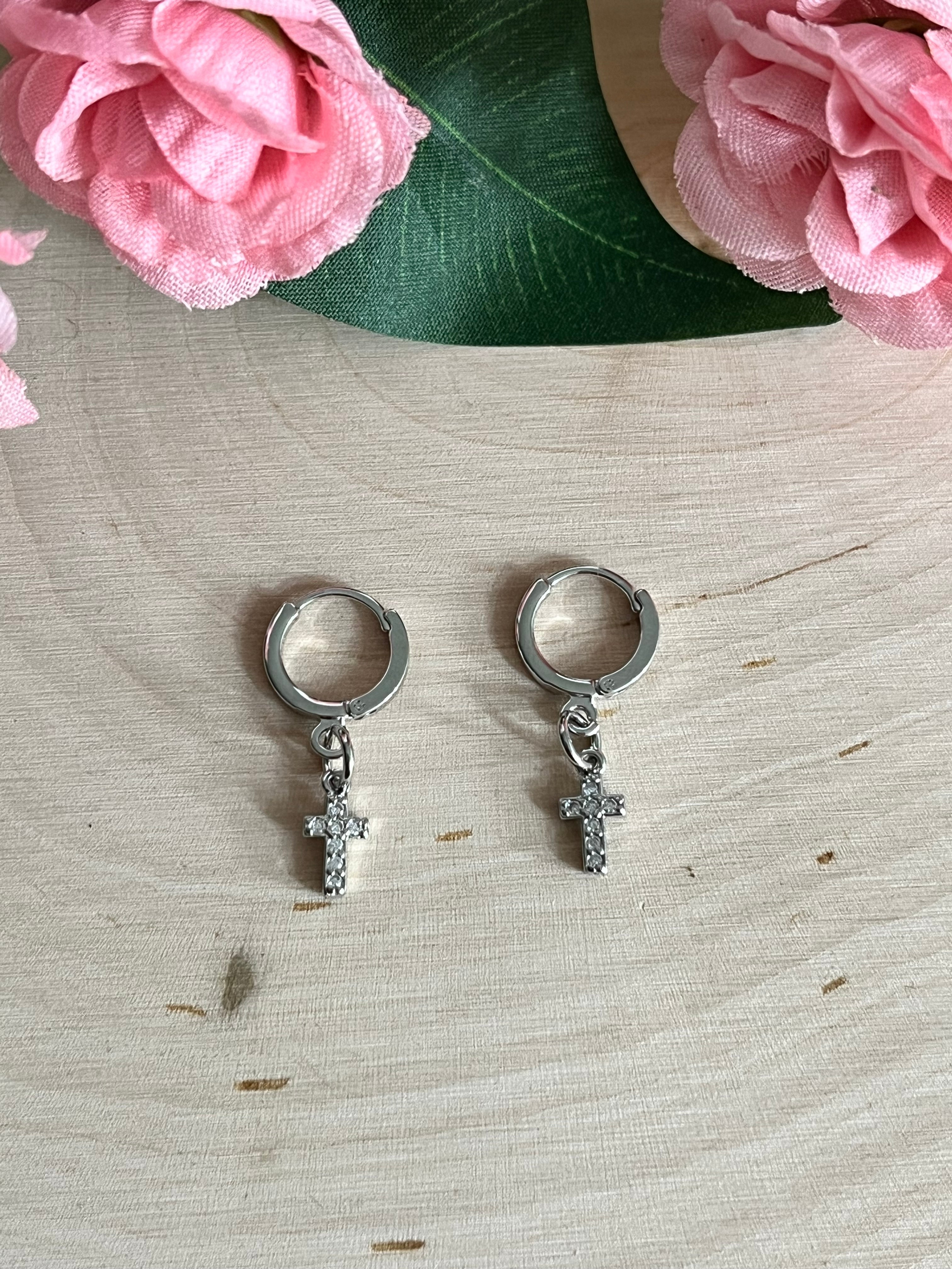 Silver huggie hoop earrings with dangling cross charms on light wooden surface