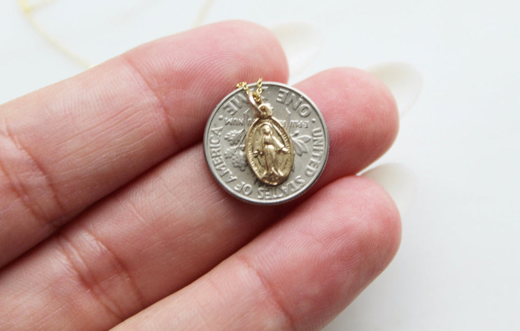 14k gold miraculous medal necklace pendant held in a hand, close-up