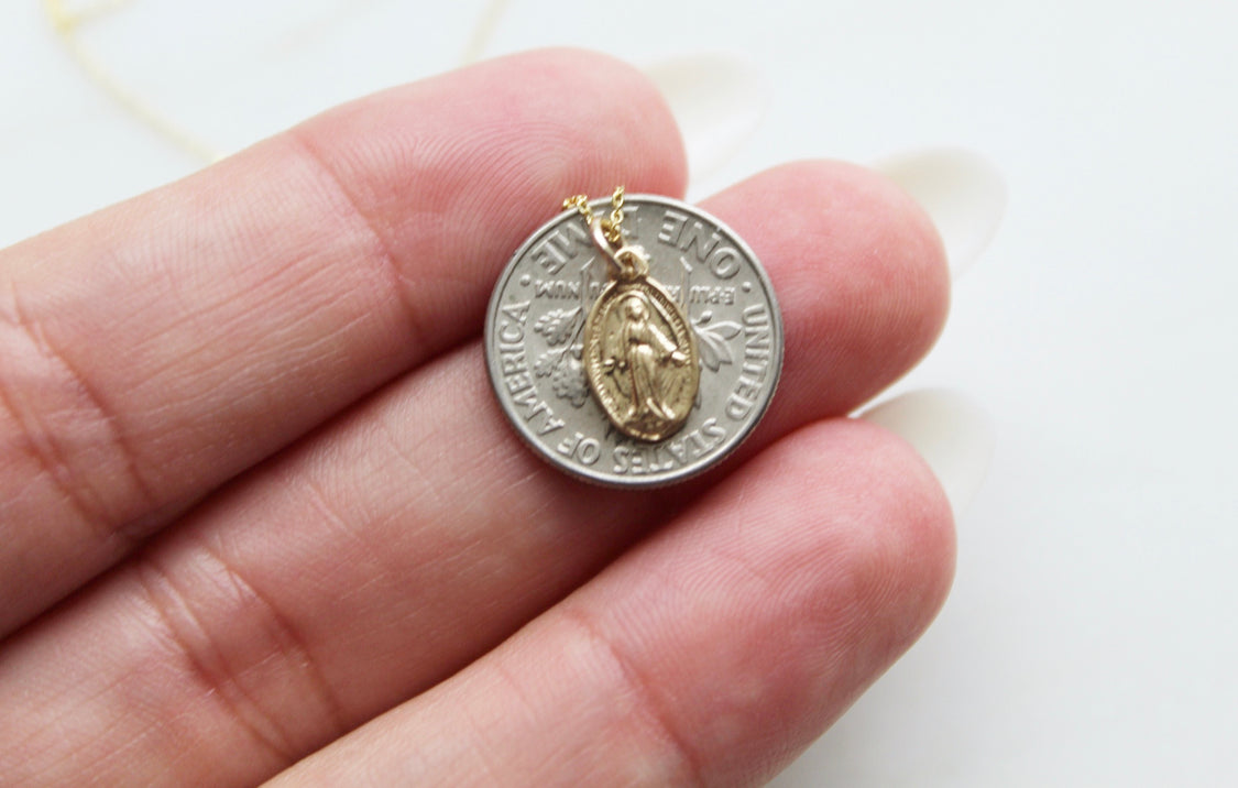 14k gold miraculous medal necklace pendant held in a hand, close-up