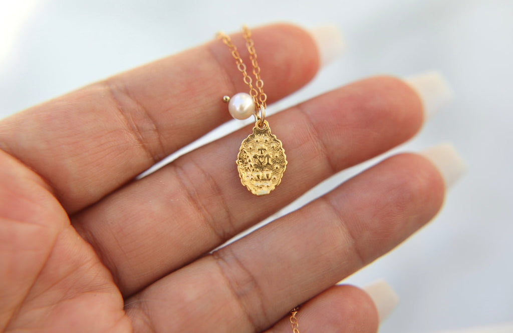Gold-tone medal necklace with pearl bead and ornate oval pendant on delicate chain
