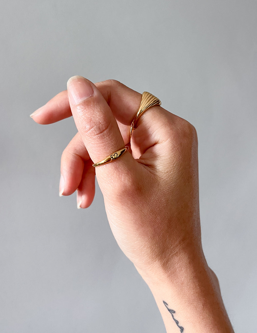 Gold love ring on finger, slim band with heart detail in side view
