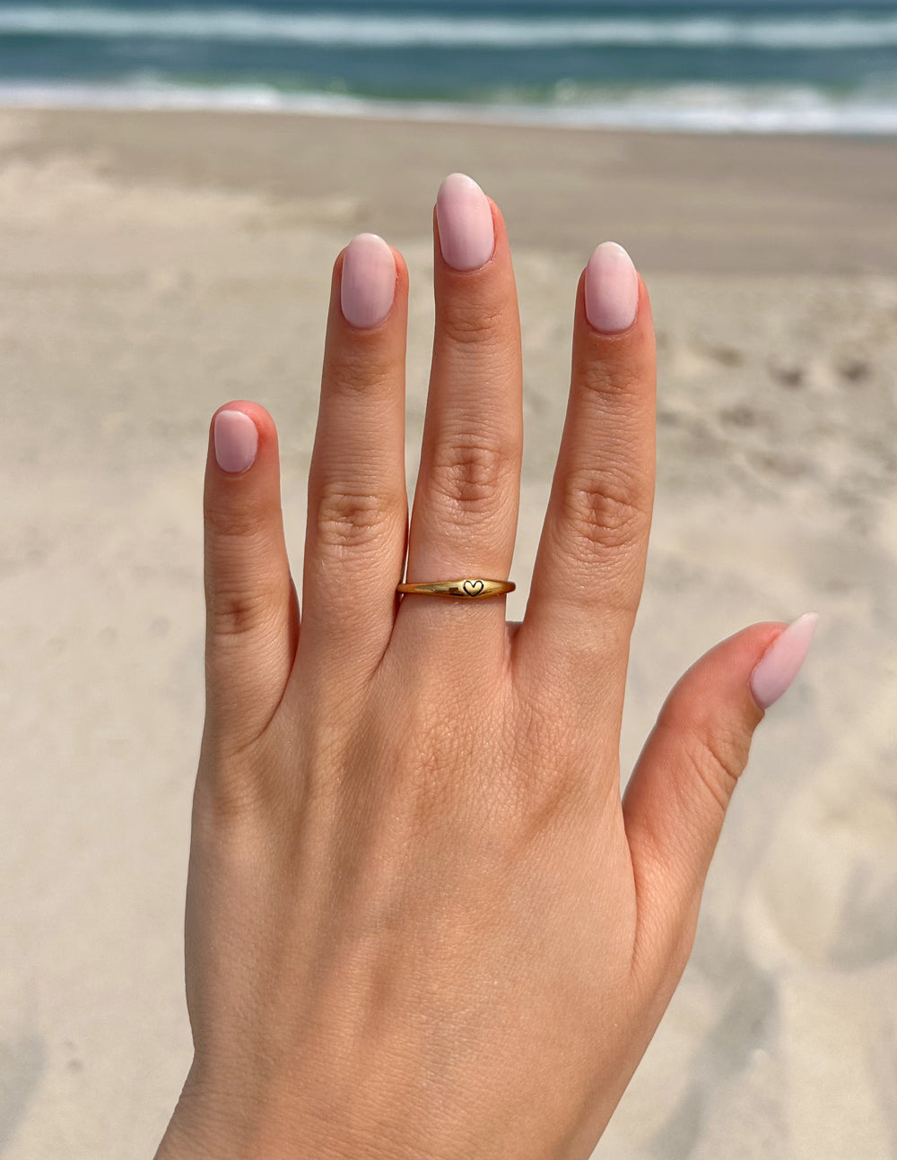 Gold love ring on hand with slim band and small heart emblem at front