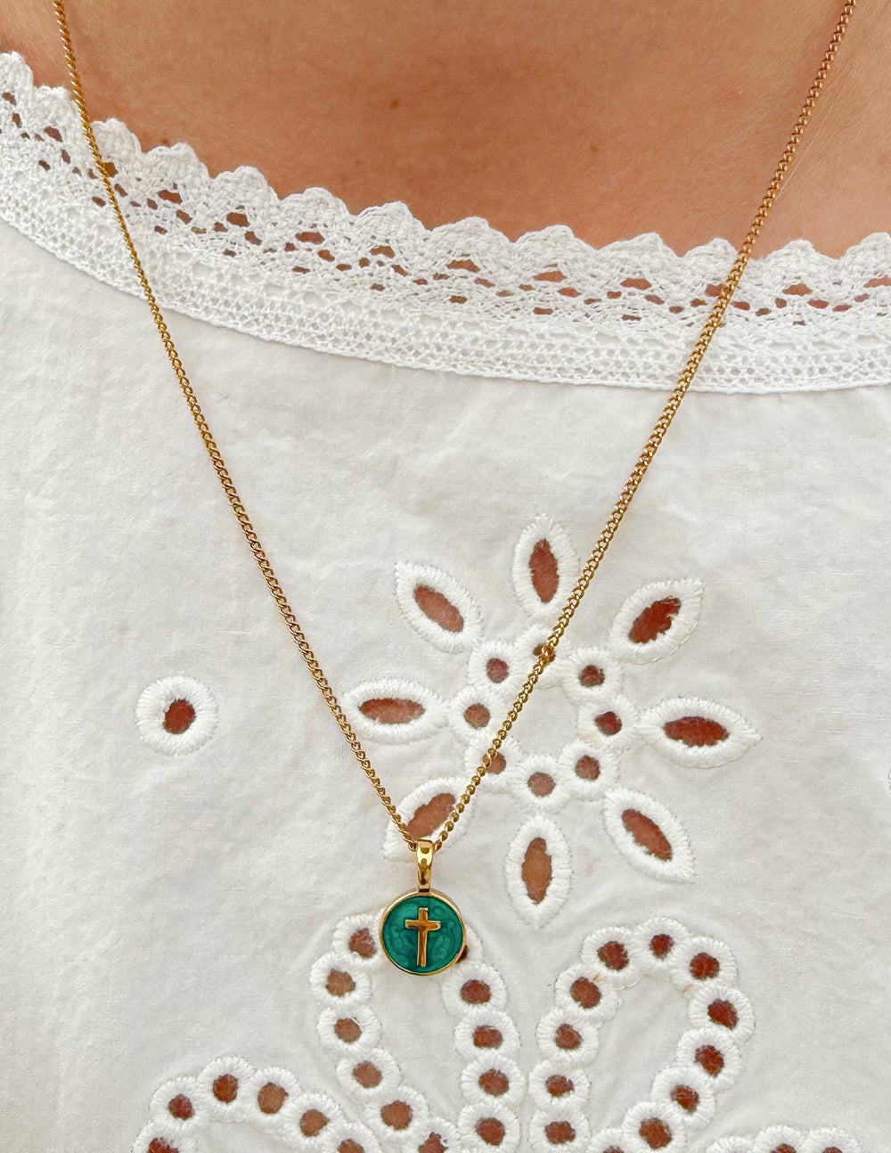 Round emerald pendant on a gold chain with an engraved cross