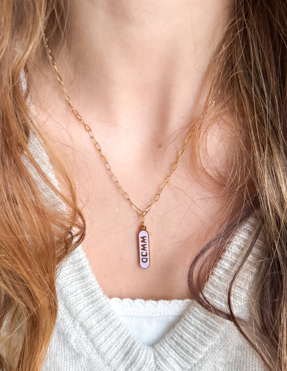 Gold-tone chain necklace with blue enamel tag pendant worn at collar