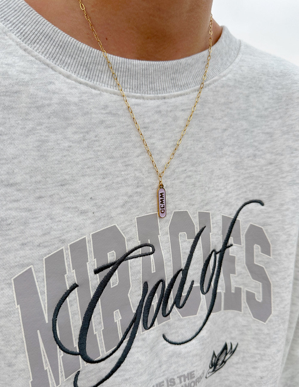 Gold-tone chain necklace with blue enamel tag pendant on chest