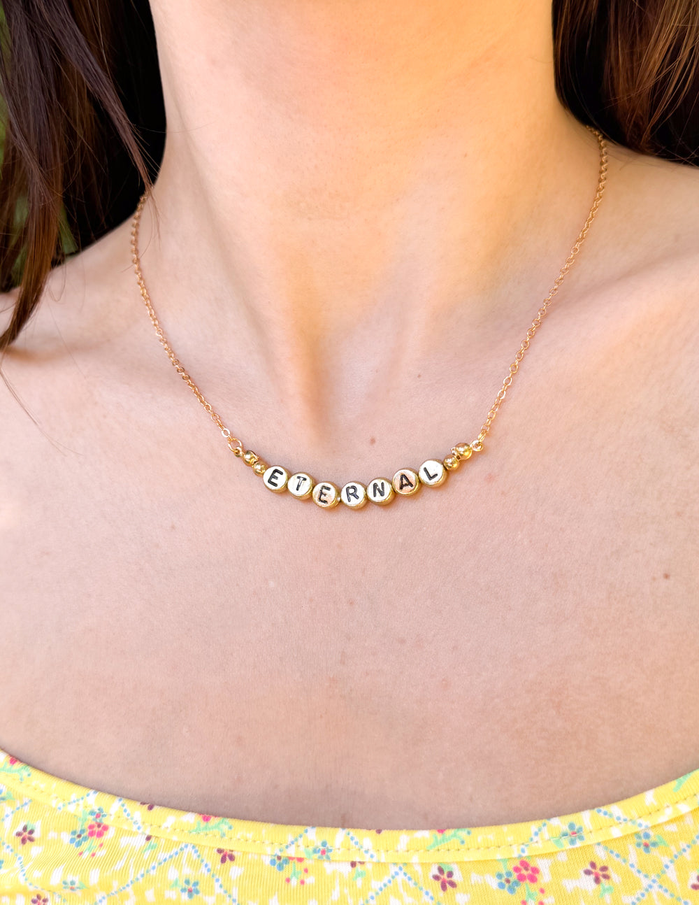 Gold-tone ETERNAL letter bead necklace with short chain close-up at collarbone