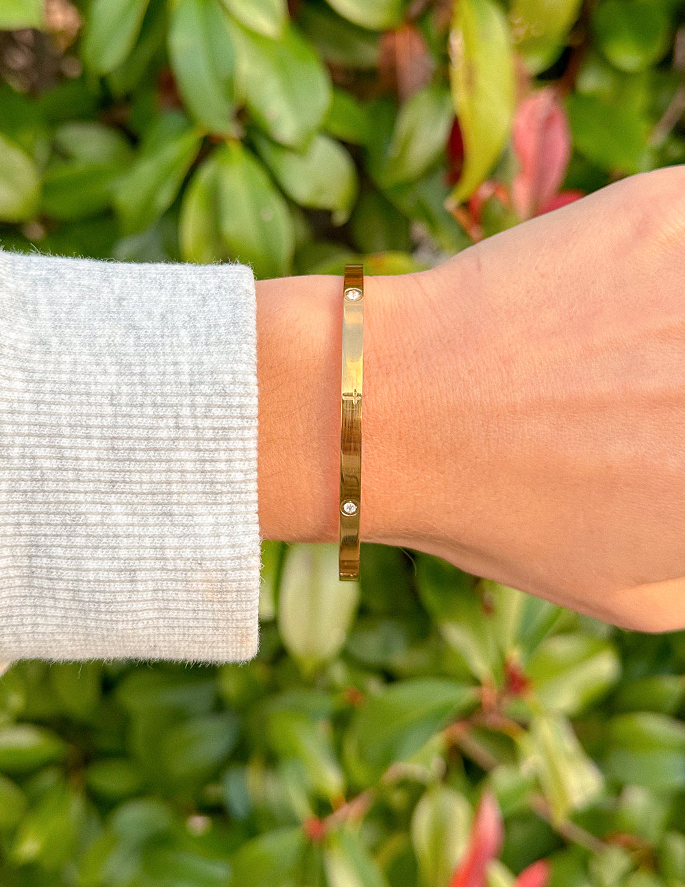 Gold-tone cuff bracelet close-up with tiny square gemstone and engraved studs