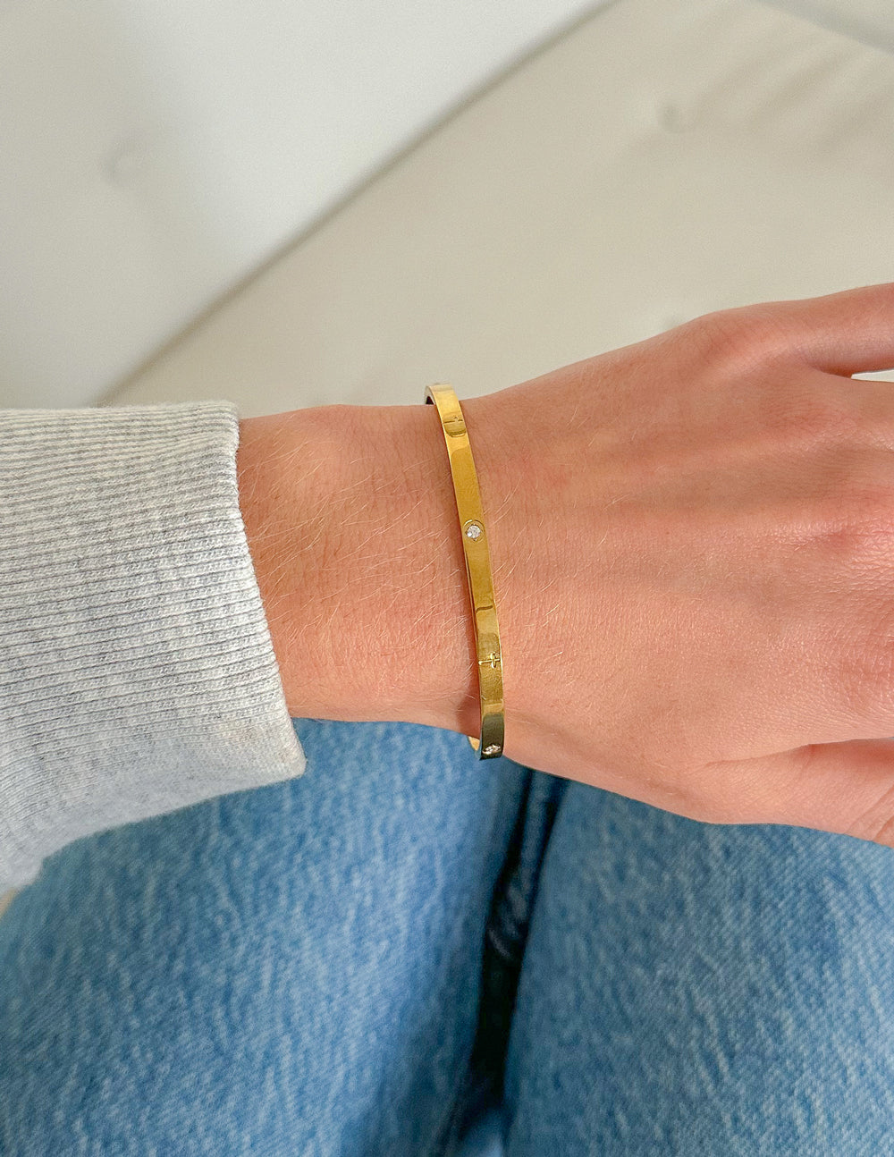 Gold-tone cuff bracelet on wrist, slim band with evenly spaced stud accents