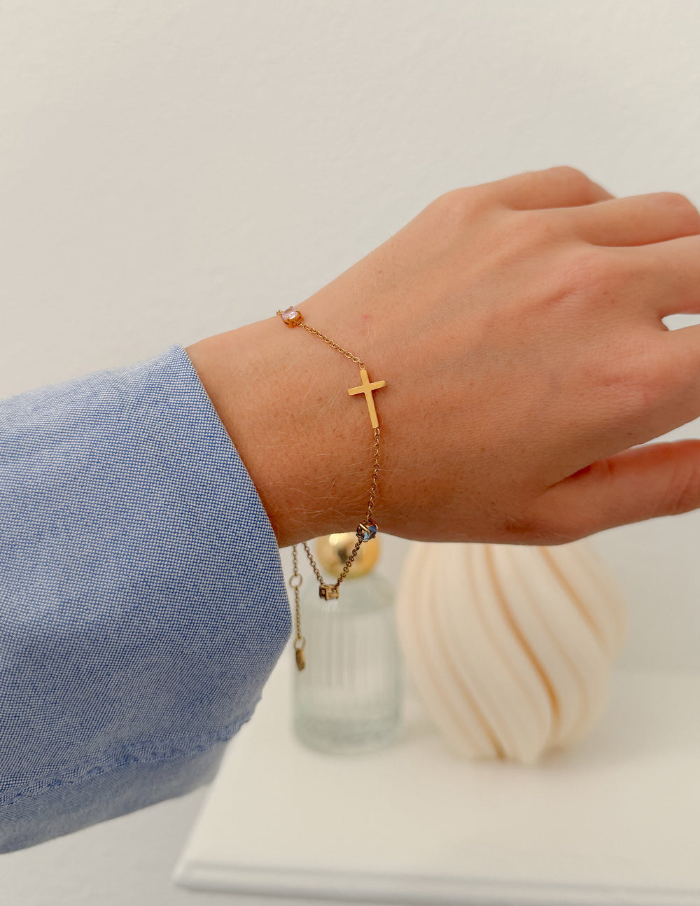 Gold cross charm bracelet on wrist, with multicolor stone details