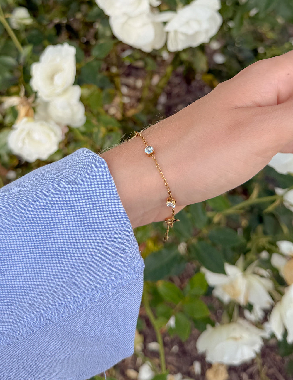 Gold link bracelet with cross charm and blue stone accent on wrist