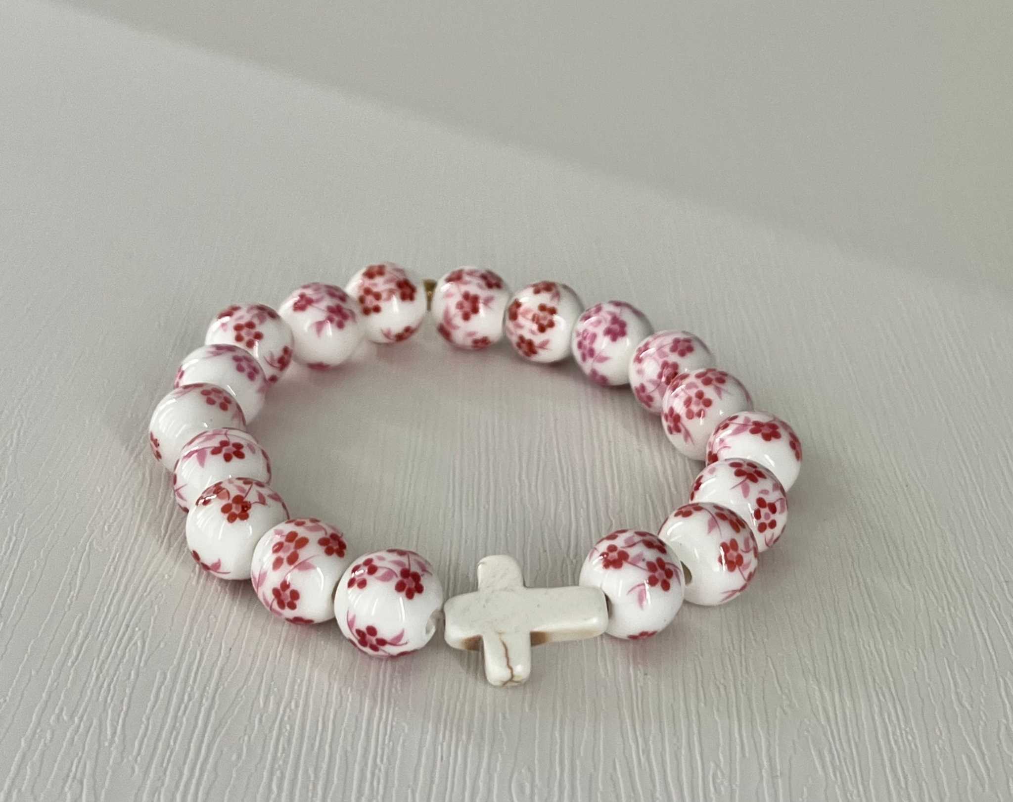 Floral-pattern beaded cross bracelet with white cross charm, centered detail.