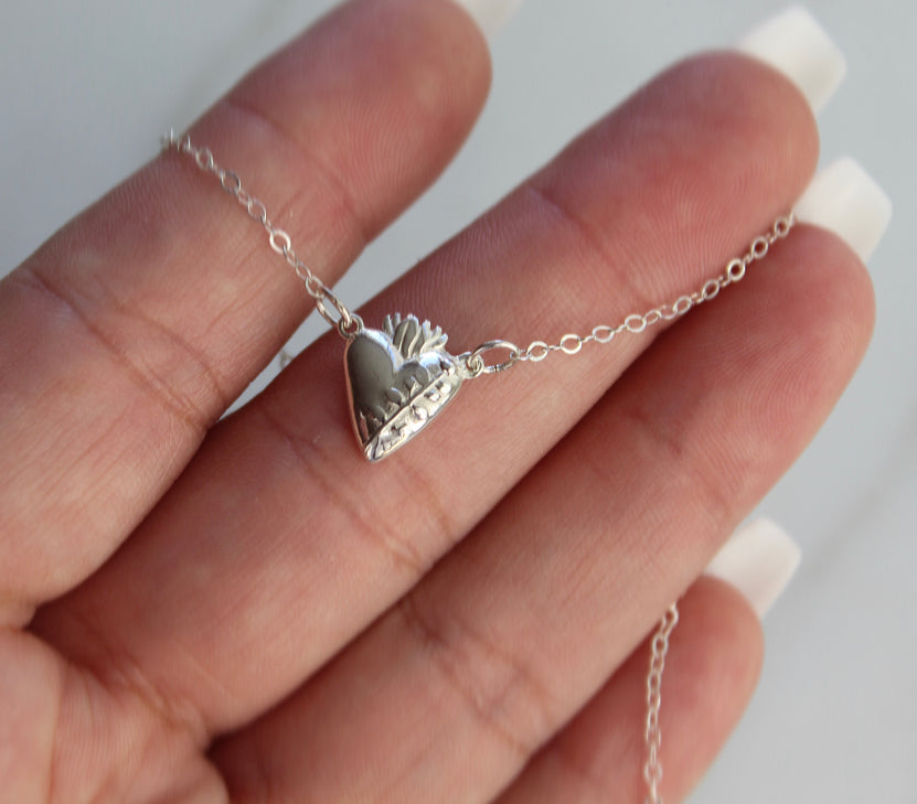 Sterling silver heart pendant necklace draped on hand, raised heart and floral details