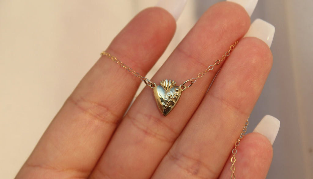 Gold-tone heart pendant necklace on open palm, centered pendant
