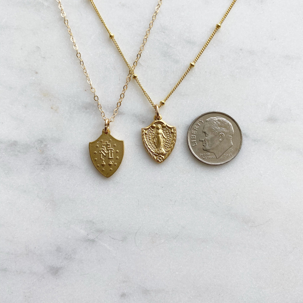Gold-tone shield pendant necklaces, two styles shown with coin for size