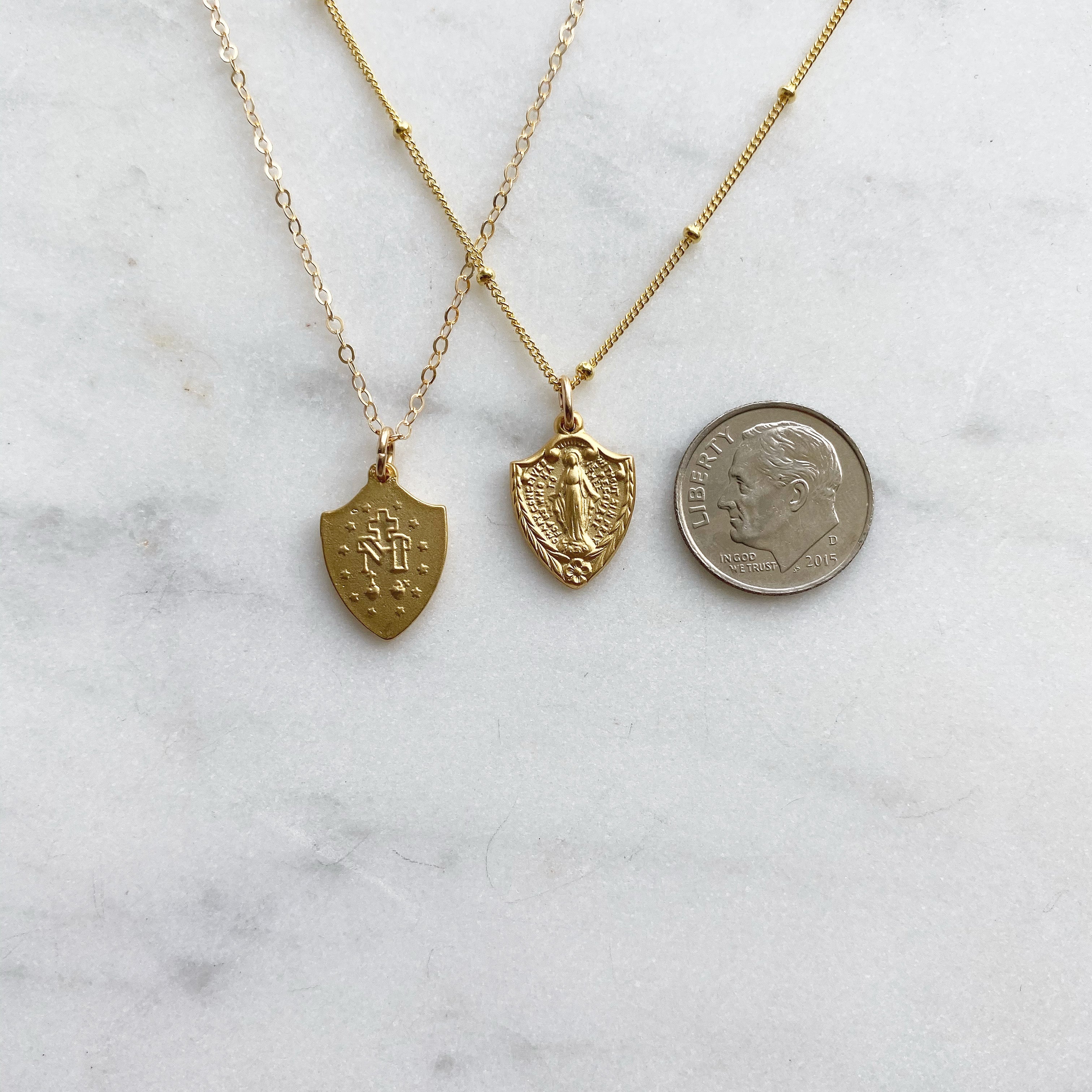 Gold-tone shield pendant necklaces, two styles shown with coin for size