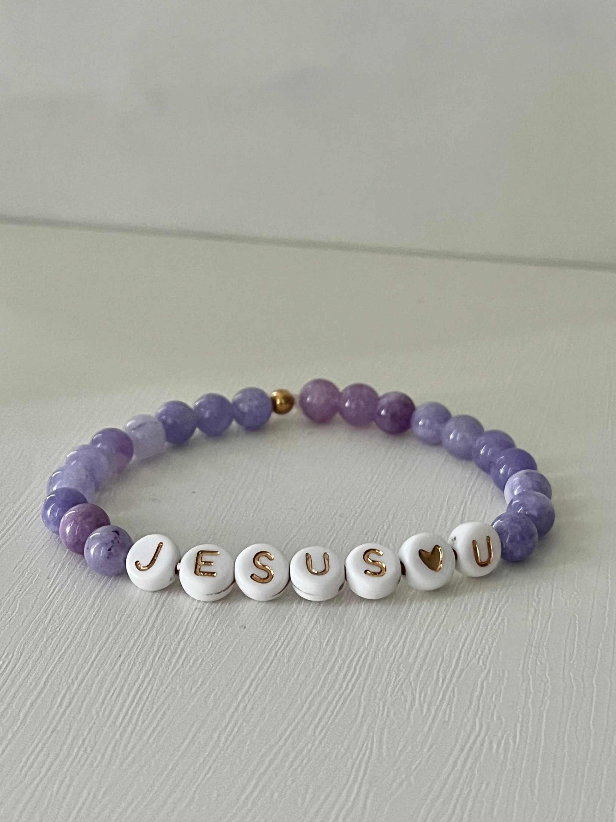 Purple beaded bracelet with white letter beads spelling "JESUS U" and small gold bead