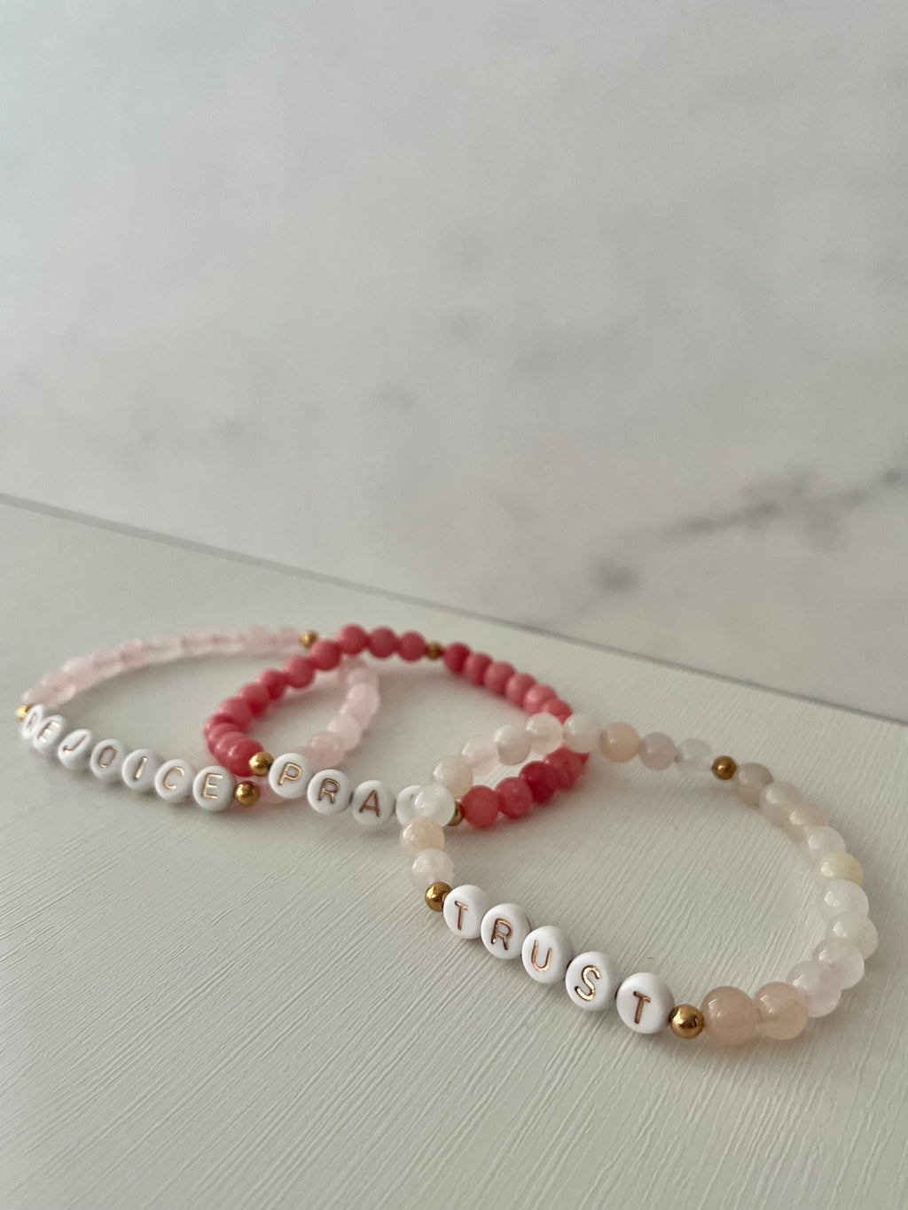 Stacked beaded bracelets with REJOICE, PRAY, and TRUST letter beads, gold accents