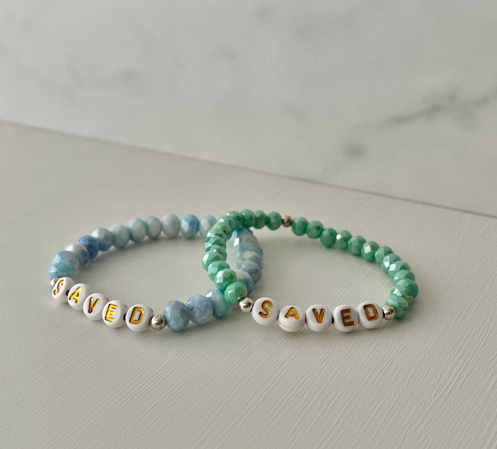 Light blue beaded bracelet with gold accents and 'SAVED' letter beads
