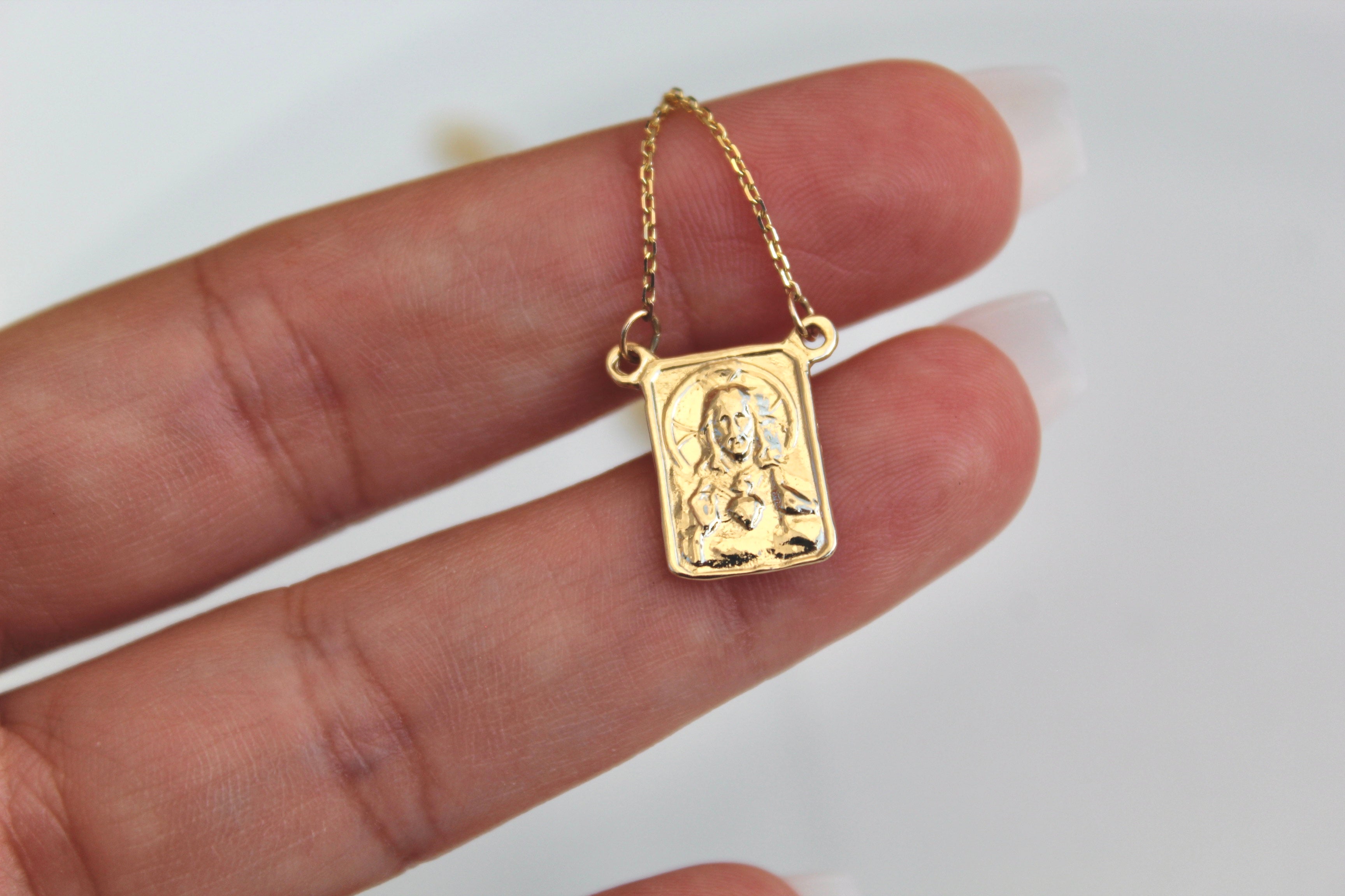 Small gold scapular pendant in palm, square embossed design on chain
