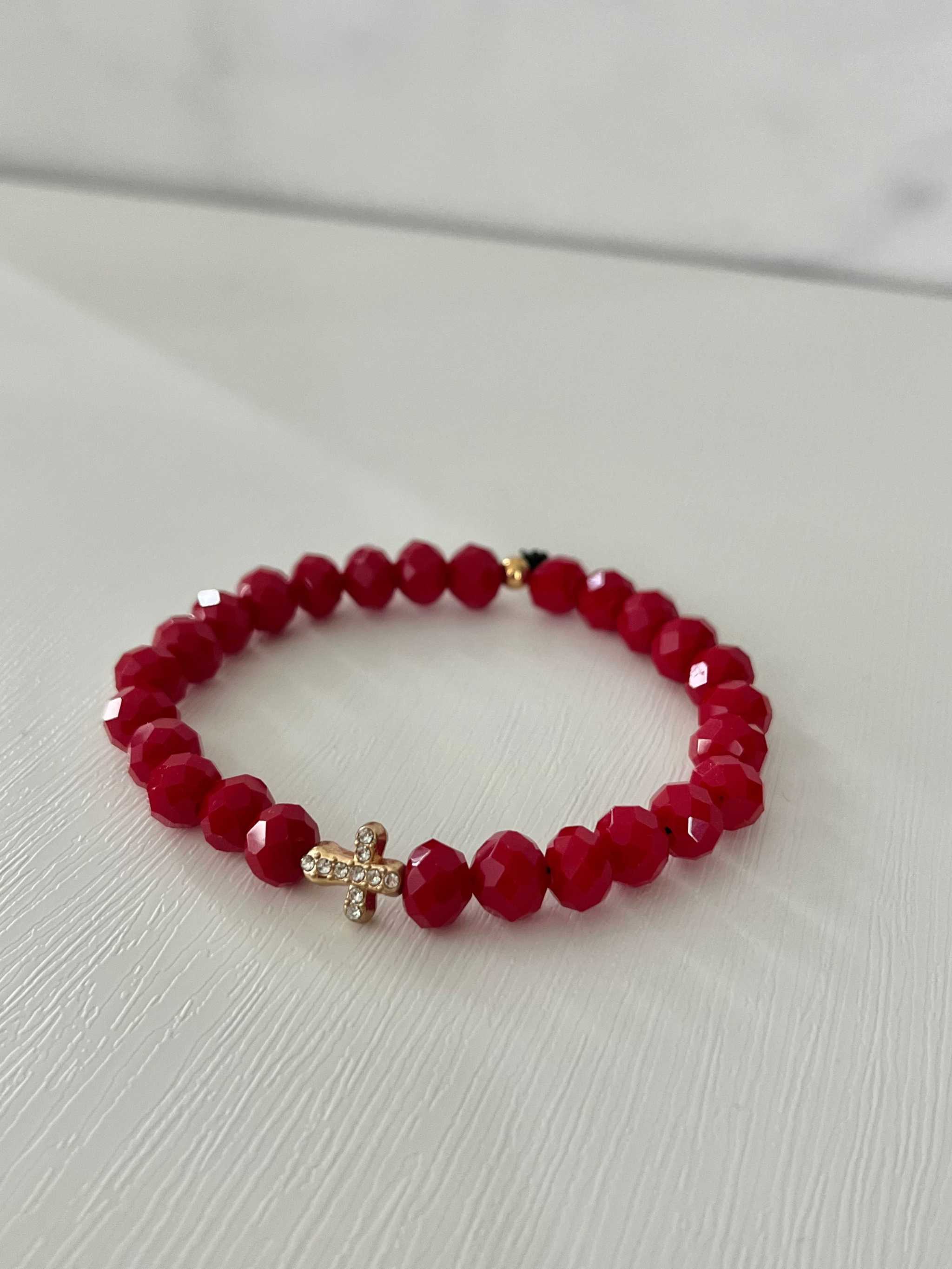 Deep red faceted bead cross bracelet with gold cross charm on loop.