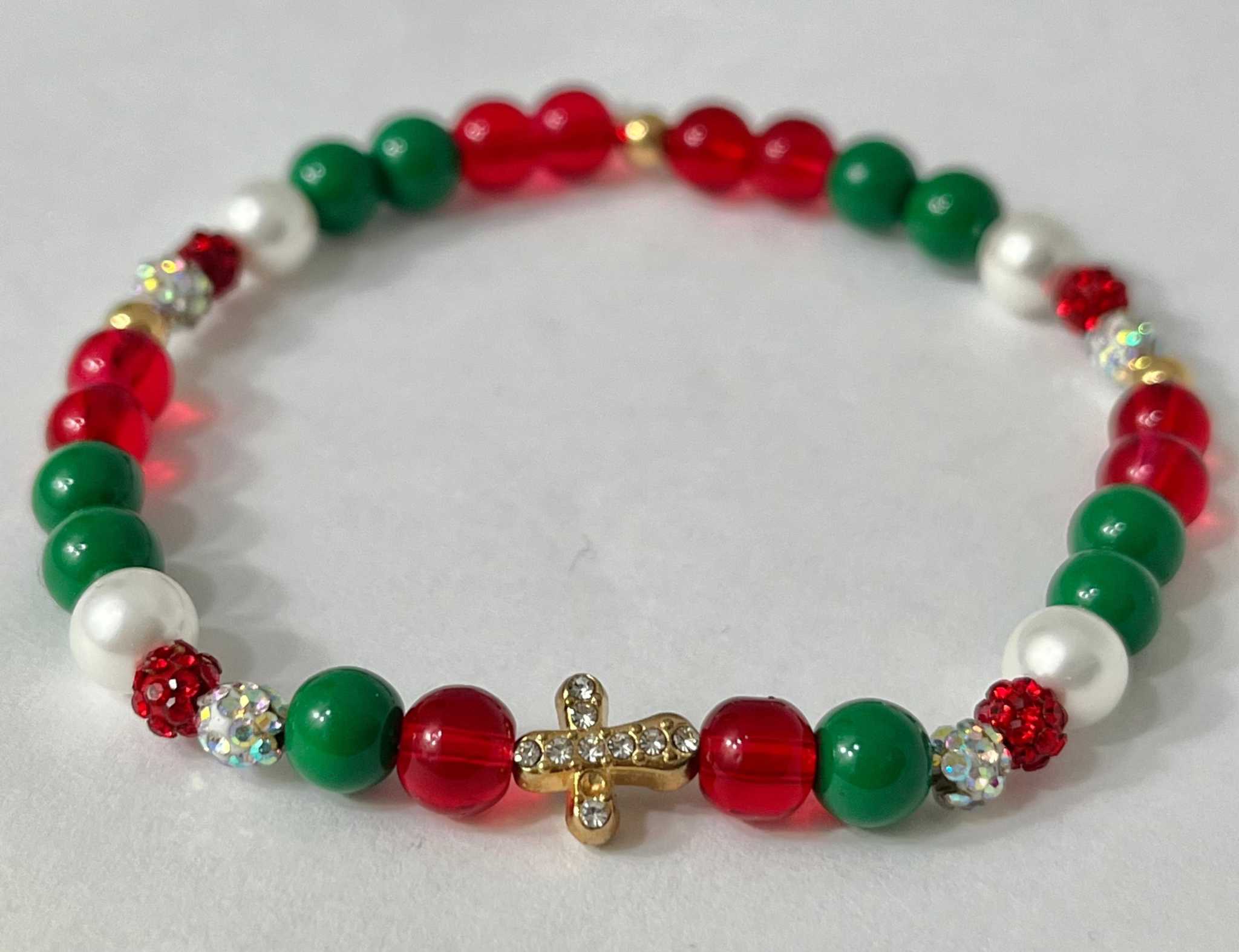 Bead bracelet with red and green beads, white spacers, and a gold jeweled cross charm