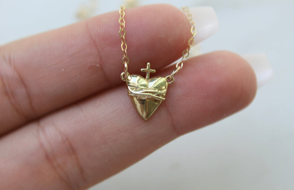 Gold-tone heart pendant necklace with crown and cross charm held in hand