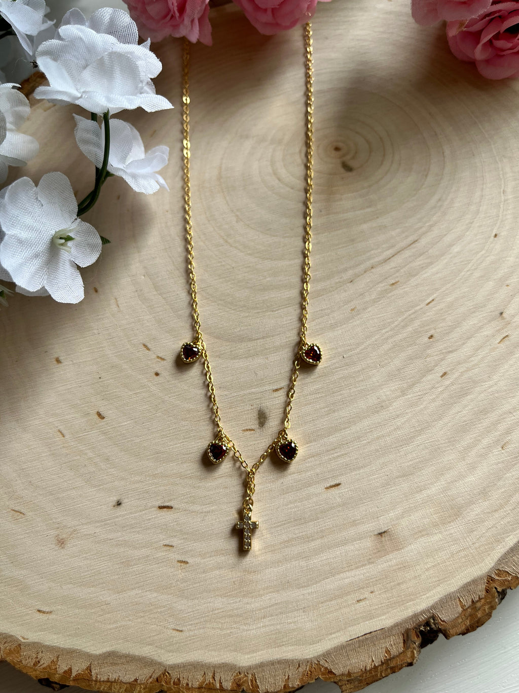 Gold charm necklace with red heart stones and gold cross pendant, top view