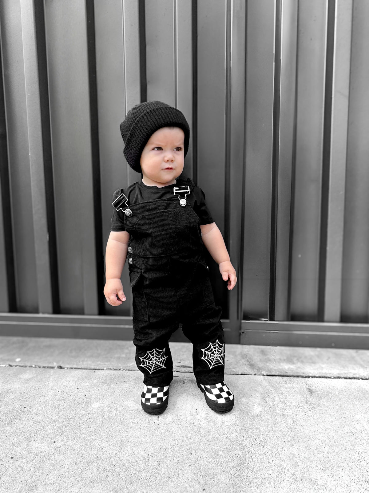 Black kids’ overalls with overall bib straps and white spiderweb patches at calves.