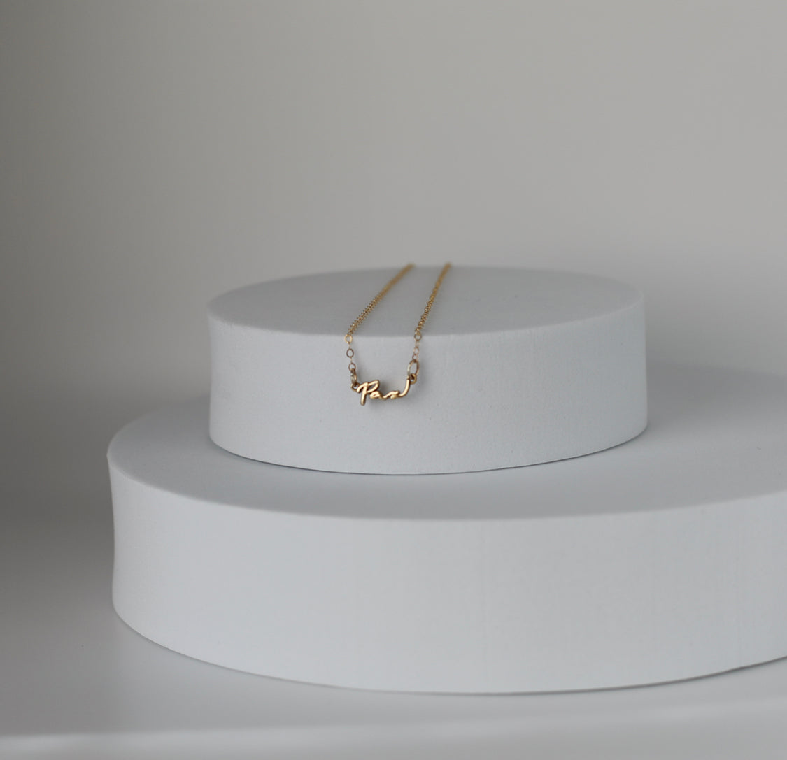 Gold Pax pendant necklace on stacked white display pedestals