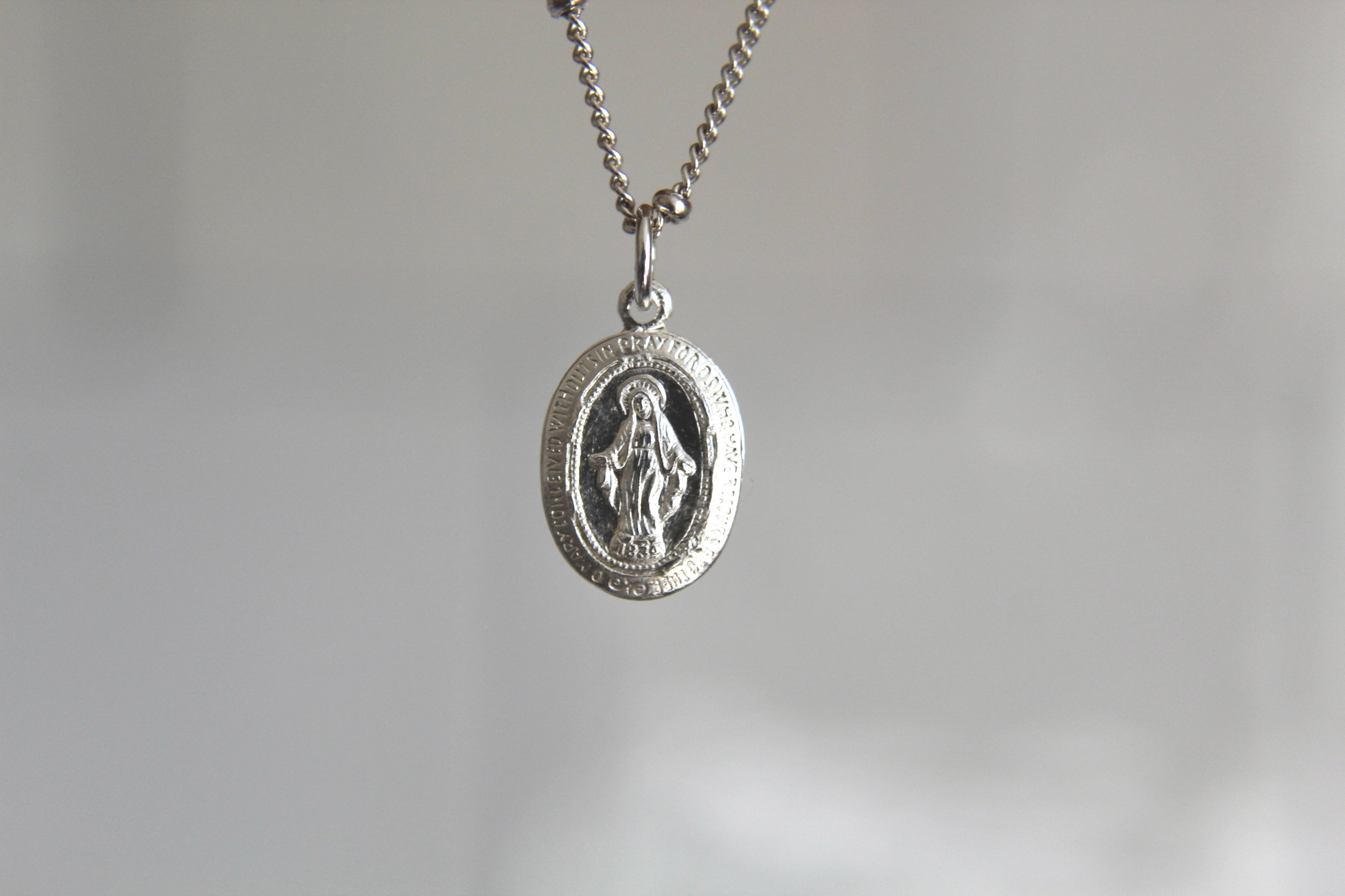 Silver miraculous medal necklace with oval pendant and figure on a chain