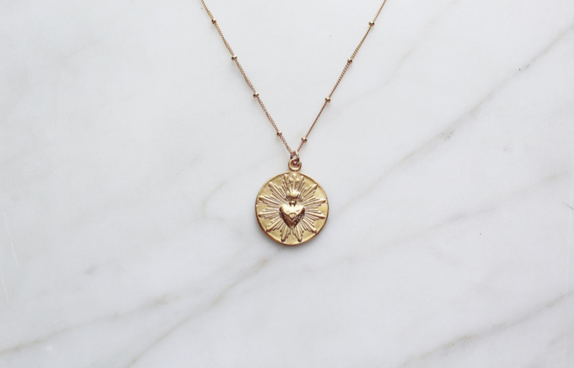 Gold-tone sacred heart coin pendant necklace with engraved center and rays