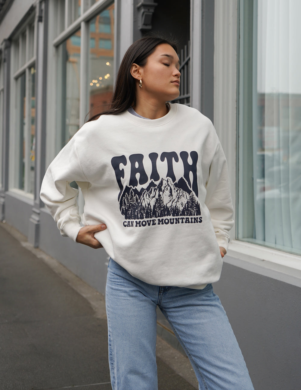 White crewneck sweatshirt with “Faith” mountain graphic and small caption text on front